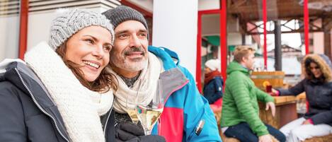 A couple embracing outdoors, with a building featuring red and white architecture in the background.