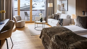 A modern hotel room with a large window, a sofa, a bed, a desk, and a chair. - ROBINSON ALPENROSE ZÜRS (Lech am Arlberg)