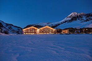A large, illuminated hotel with multiple floors and a prominent mountain in the background. - ROBINSON ALPENROSE ZÜRS (Lech am Arlberg)