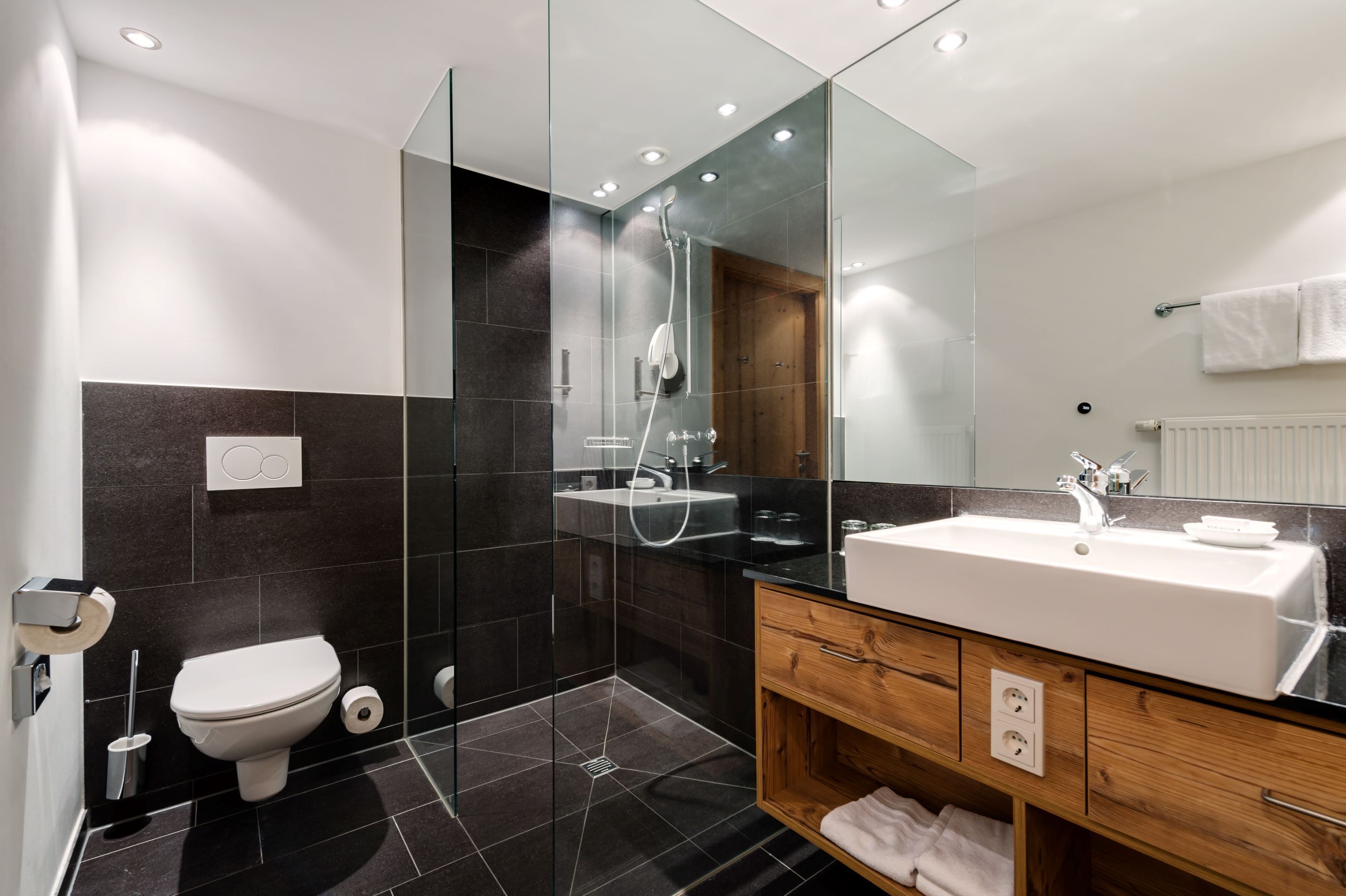 Ein modernes Badezimmer mit einer in Glas abgeschlossenen Dusche, einem weißen Waschbecken und einem hölzernen Waschtisch.