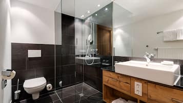 Ein modernes Badezimmer mit einer in Glas abgeschlossenen Dusche, einem weißen Waschbecken und einem hölzernen Waschtisch.