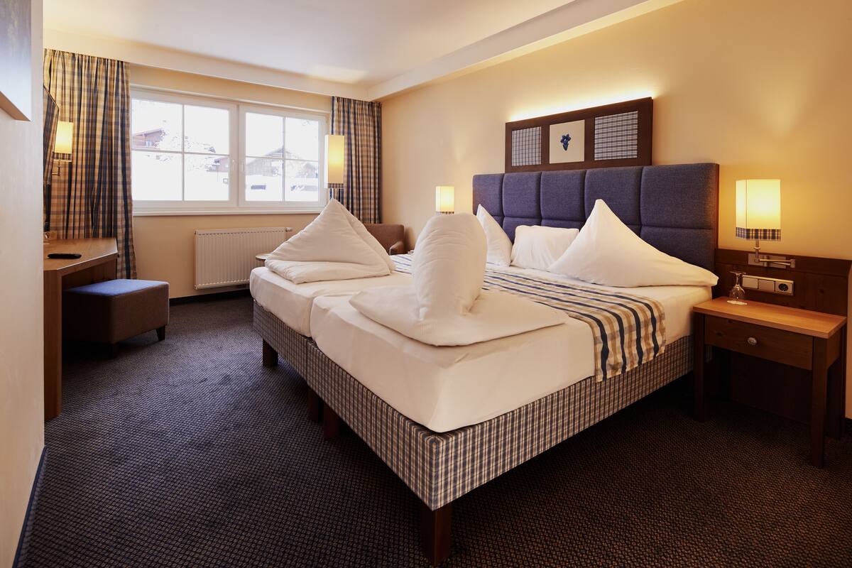 Una habitación de hotel con una cama grande, un escritorio, una silla y una ventana con cortinas.