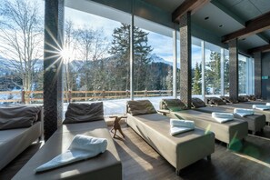 A spa area with multiple massage tables, a wooden floor, and large windows offering a mountain view. - Arosa Alpine Club  (Arosa)