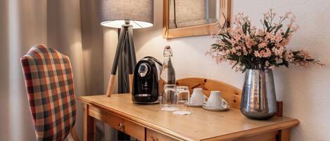 A wooden desk with a lamp, a coffee maker, a vase with flowers, and a chair with a plaid cushion.