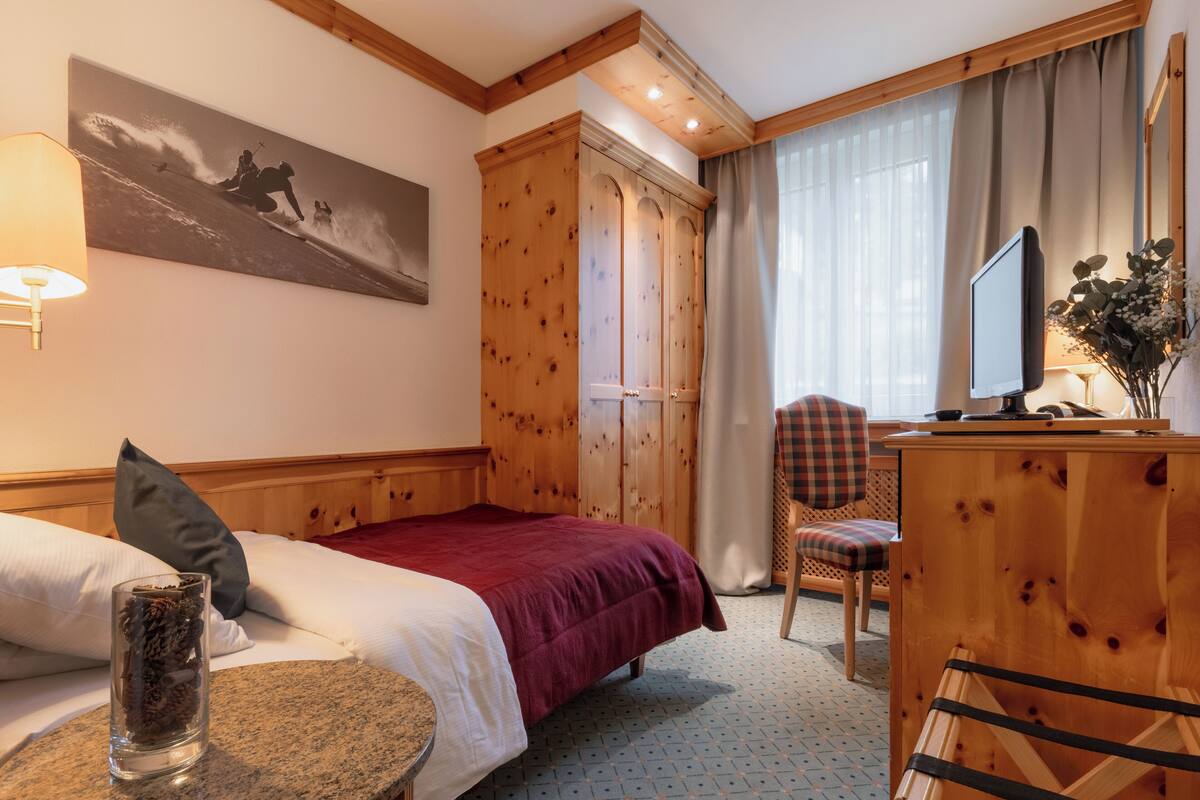 Una habitació d'hotel amb un llit, una taula de treball, una televisió, una cadira i un quadre a la paret.