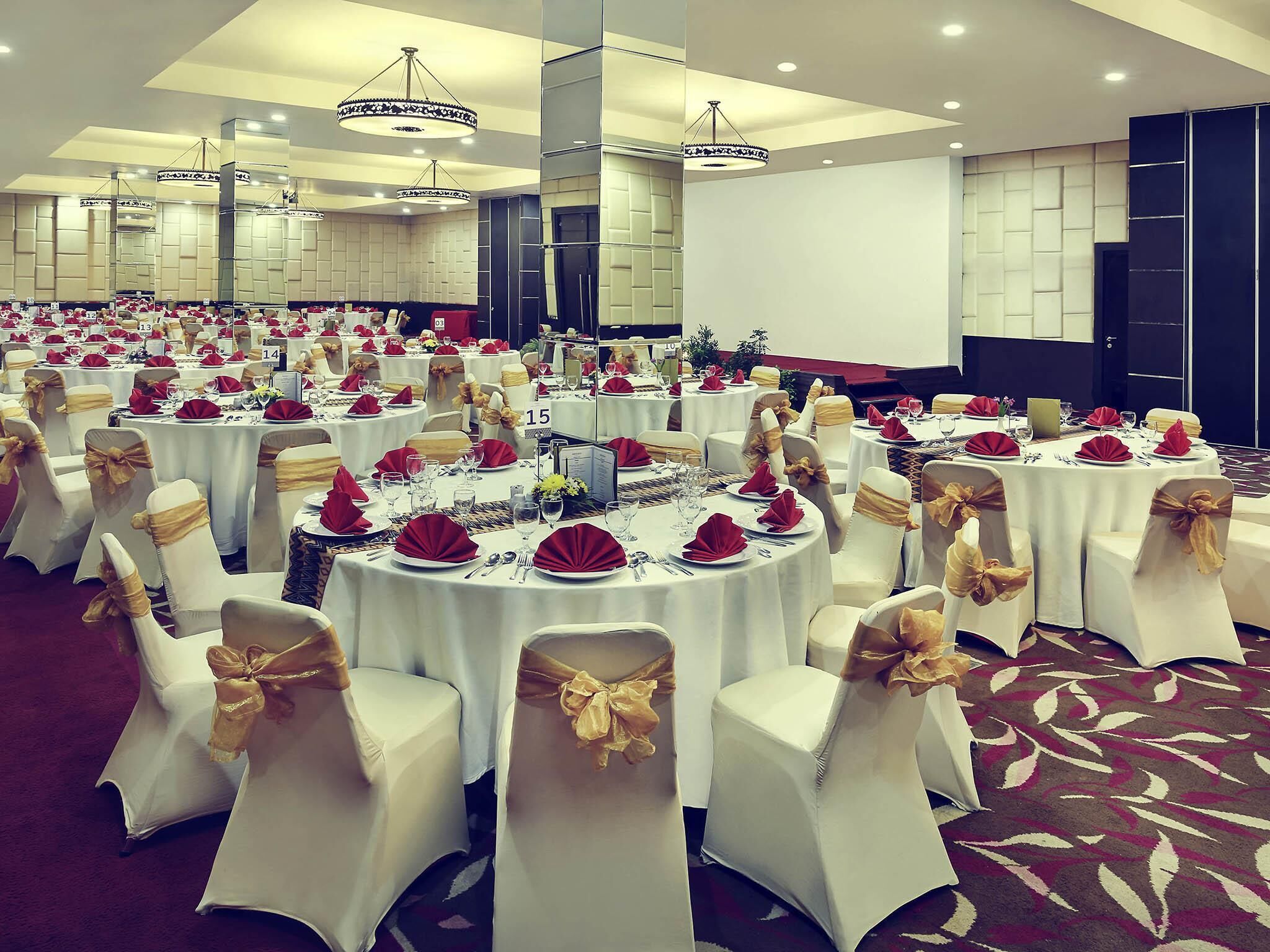 A banquet hall with round tables, white chairs with gold sashes, and chandeliers.