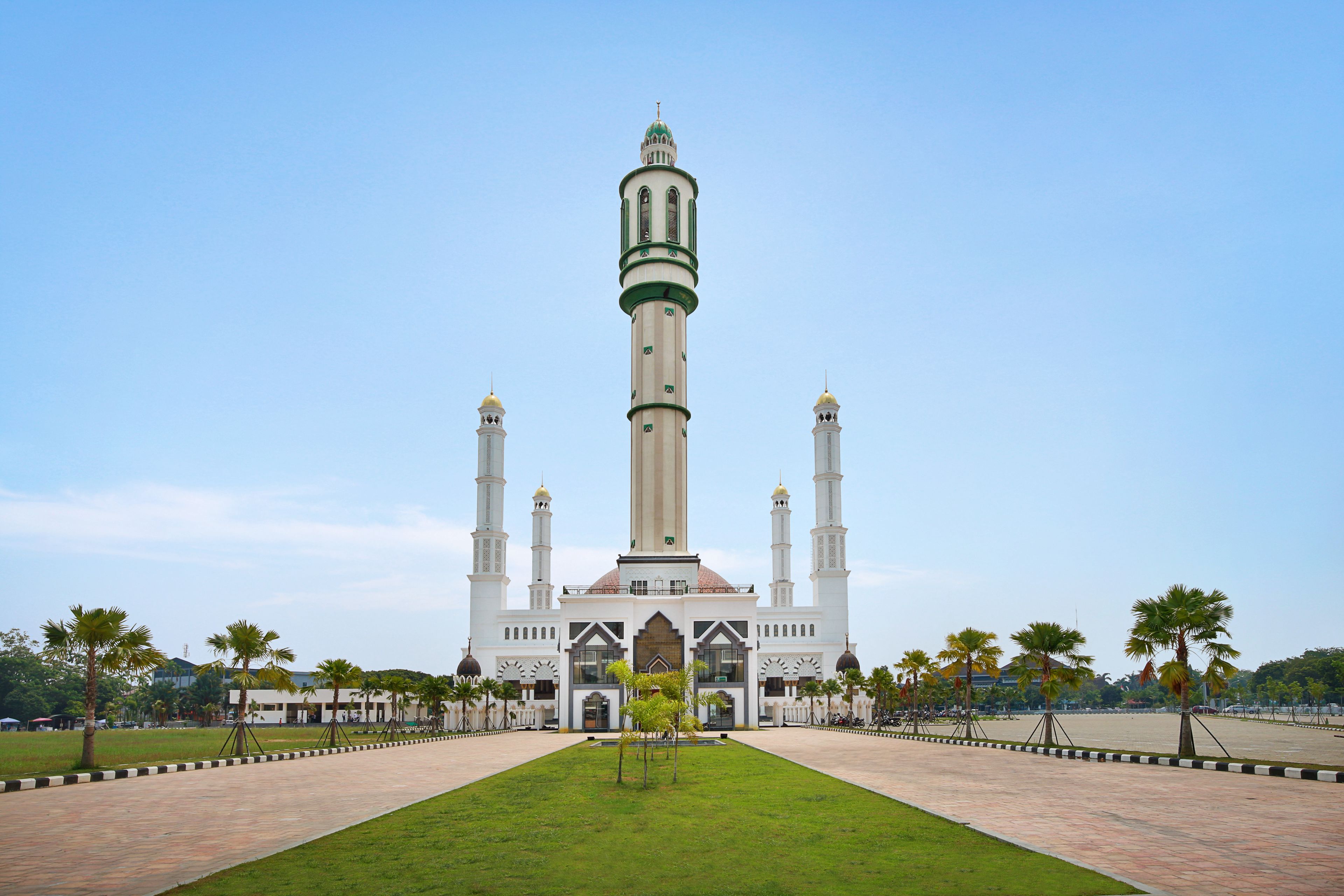 Eine große Moschee mit einem hohen Minarett, einem zentralen Innenhof und Palmen.