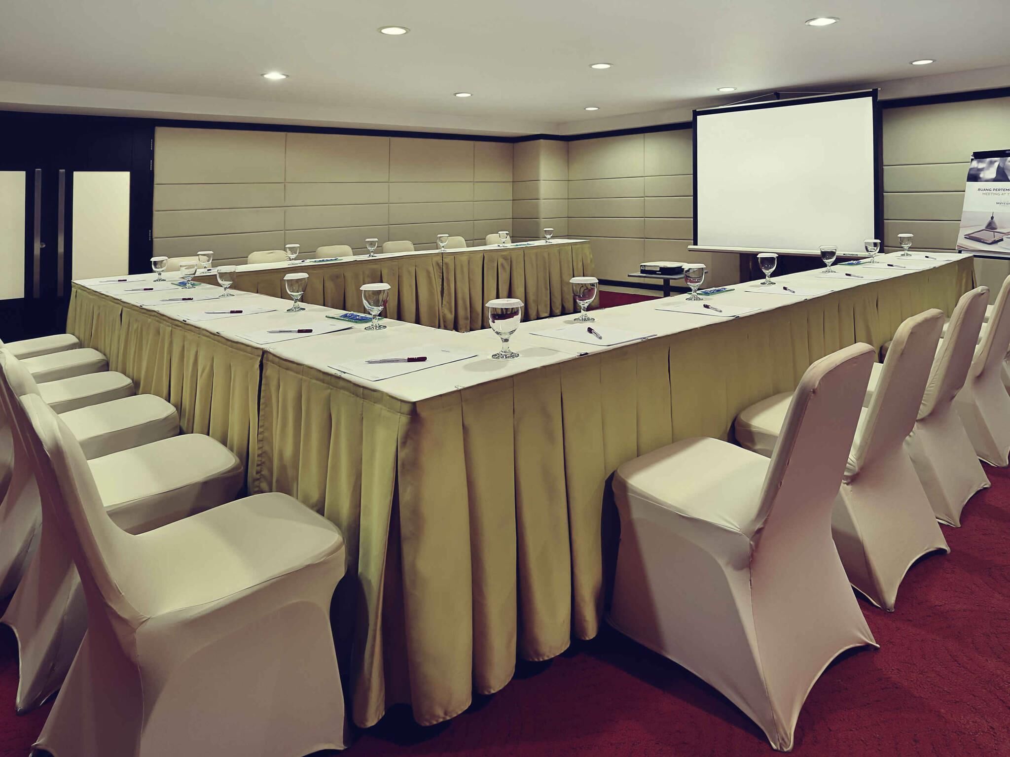 A conference room with a long table, chairs, and a projector screen.