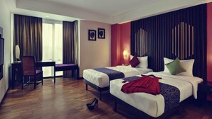 Une chambre d’hôtel avec deux lits, un bureau, une chaise et une grande fenêtre avec des rideaux.