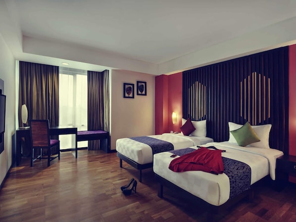 A hotel room with two beds, a desk, a chair, and a large window with curtains.
