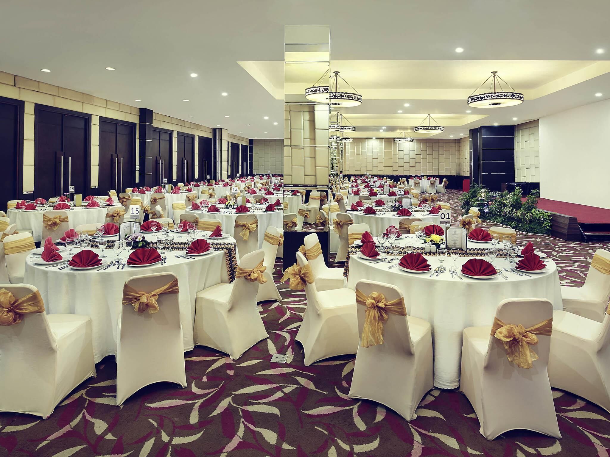 A banquet hall with round tables, white chairs with gold sashes, and chandeliers.