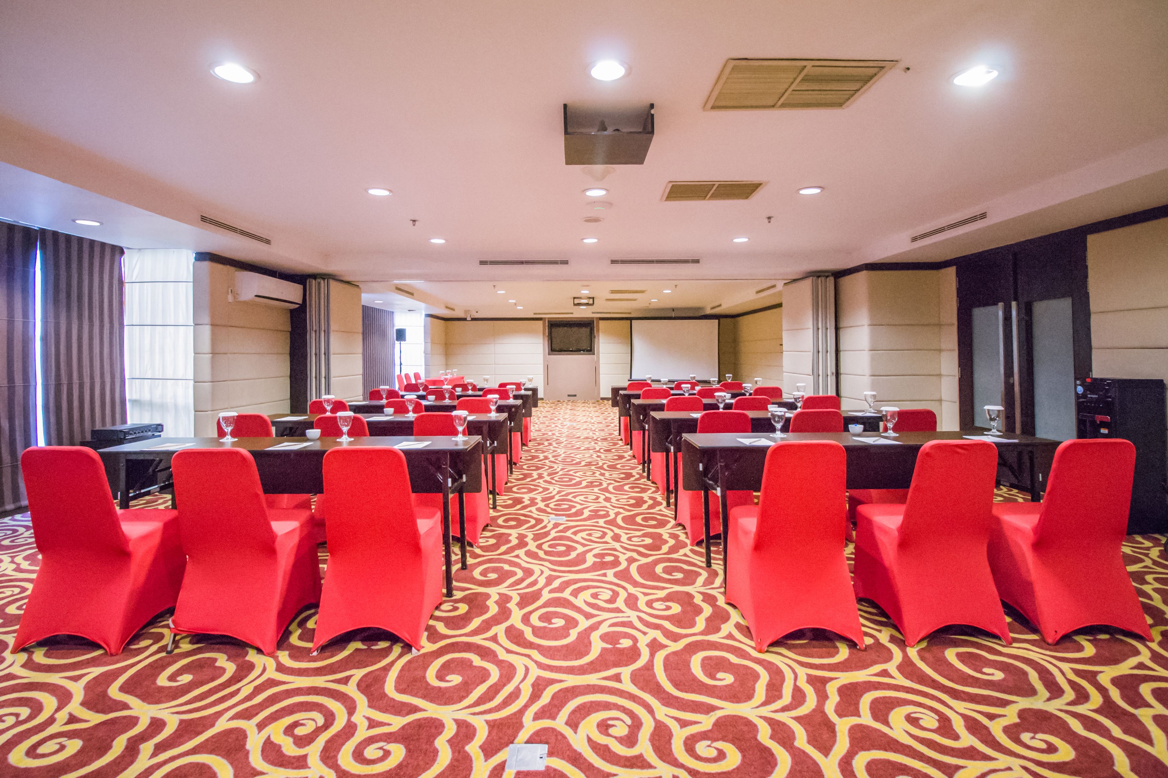 A conference room with red chairs, a patterned carpet, and a long table.