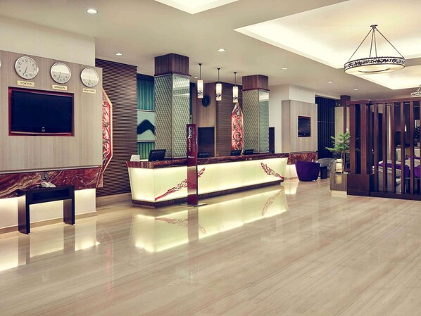 A modern hotel lobby with a reception desk, clocks displaying Tokyo, London, and New York times, and a large chandelier. - Mercure Pontianak City Center (Pontianak)