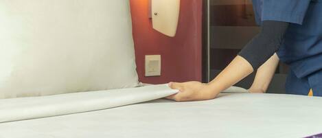 Una habitación de hotel con una cama bien hecha, una lámpara fijada a la pared y un enchufe visible.