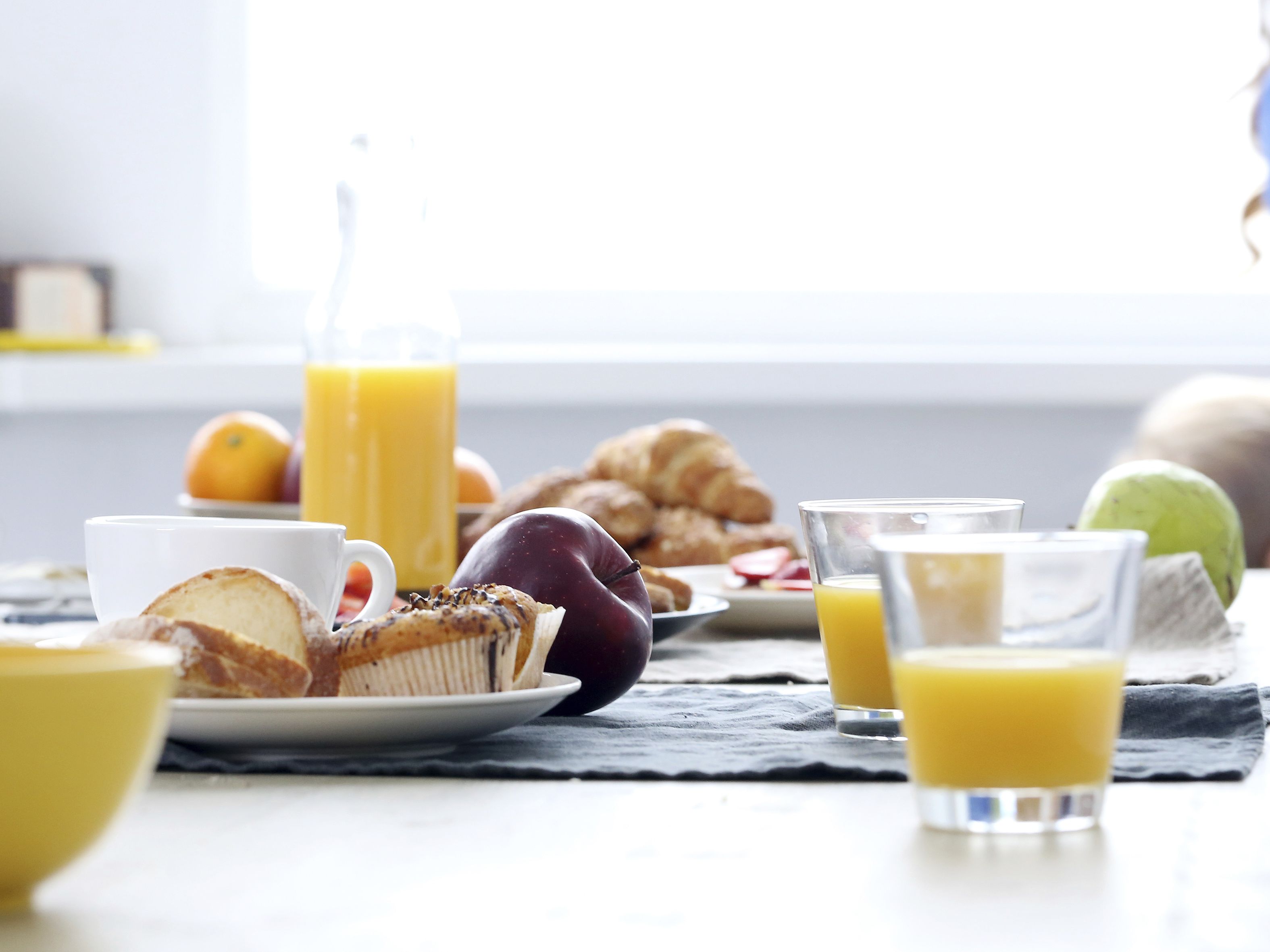 A breakfast setting with a croissant, a muffin, a glass of orange juice, and a plate of fruit.