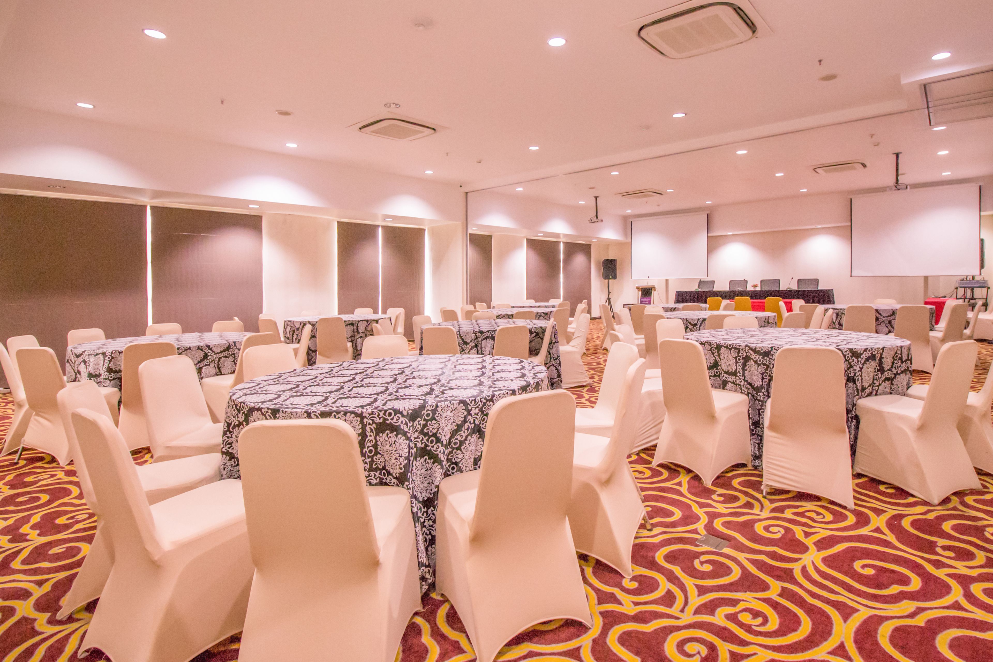 A conference room with round tables, white chairs, and a carpeted floor.