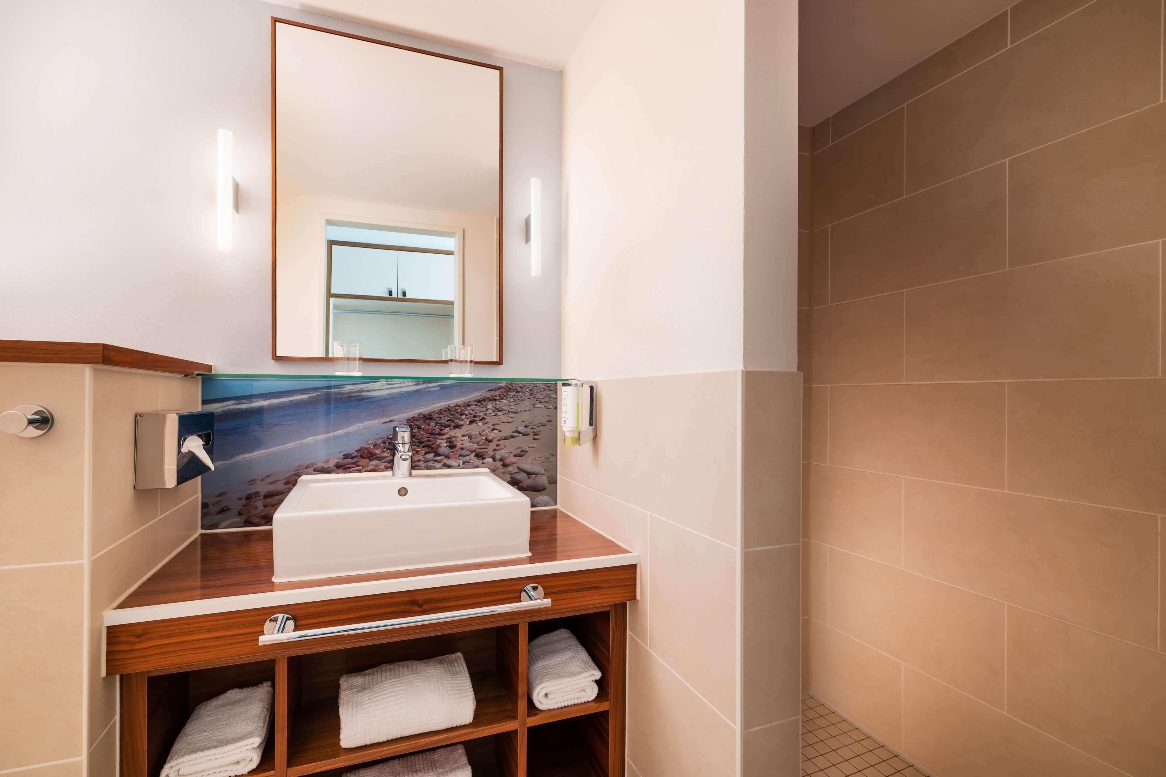A bathroom with a sink, mirror, towel rack, and a tiled wall.