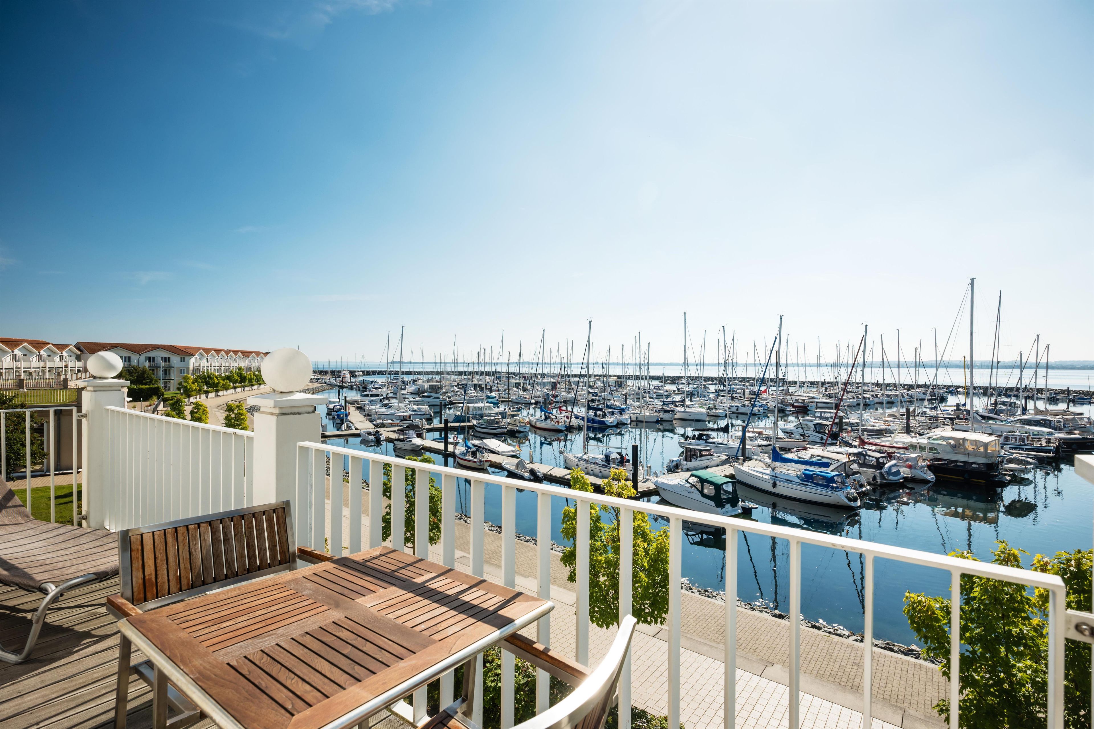 A marina with numerous boats docked, a wooden deck with a table and chairs, and a clear blue sky.