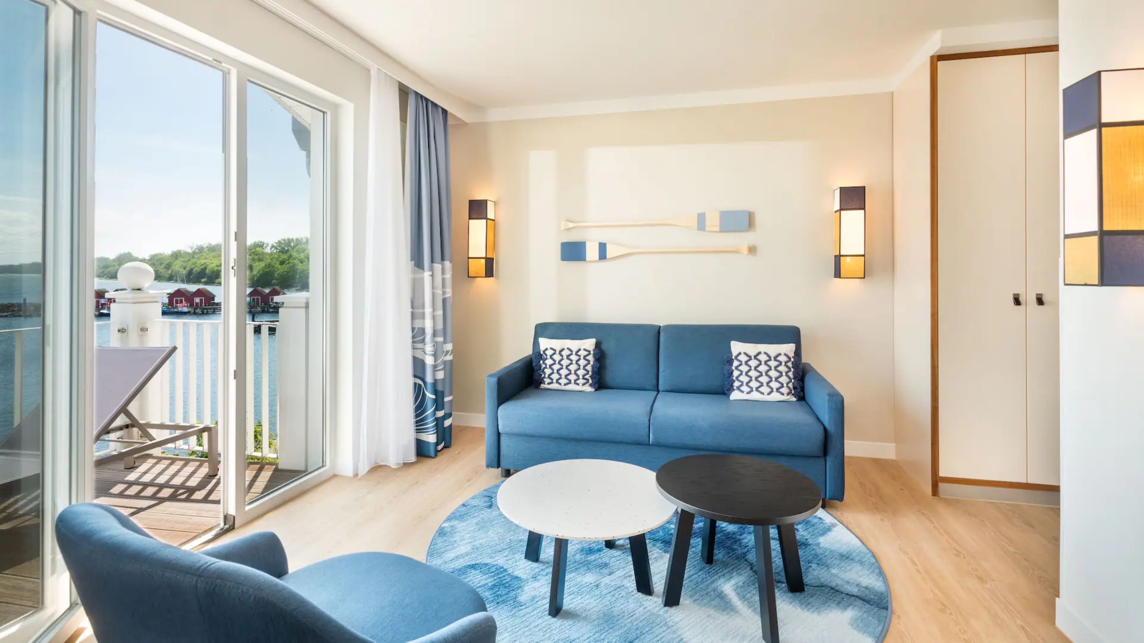 A modern living room with a blue sofa, two round tables, and a view of a balcony with a pool.