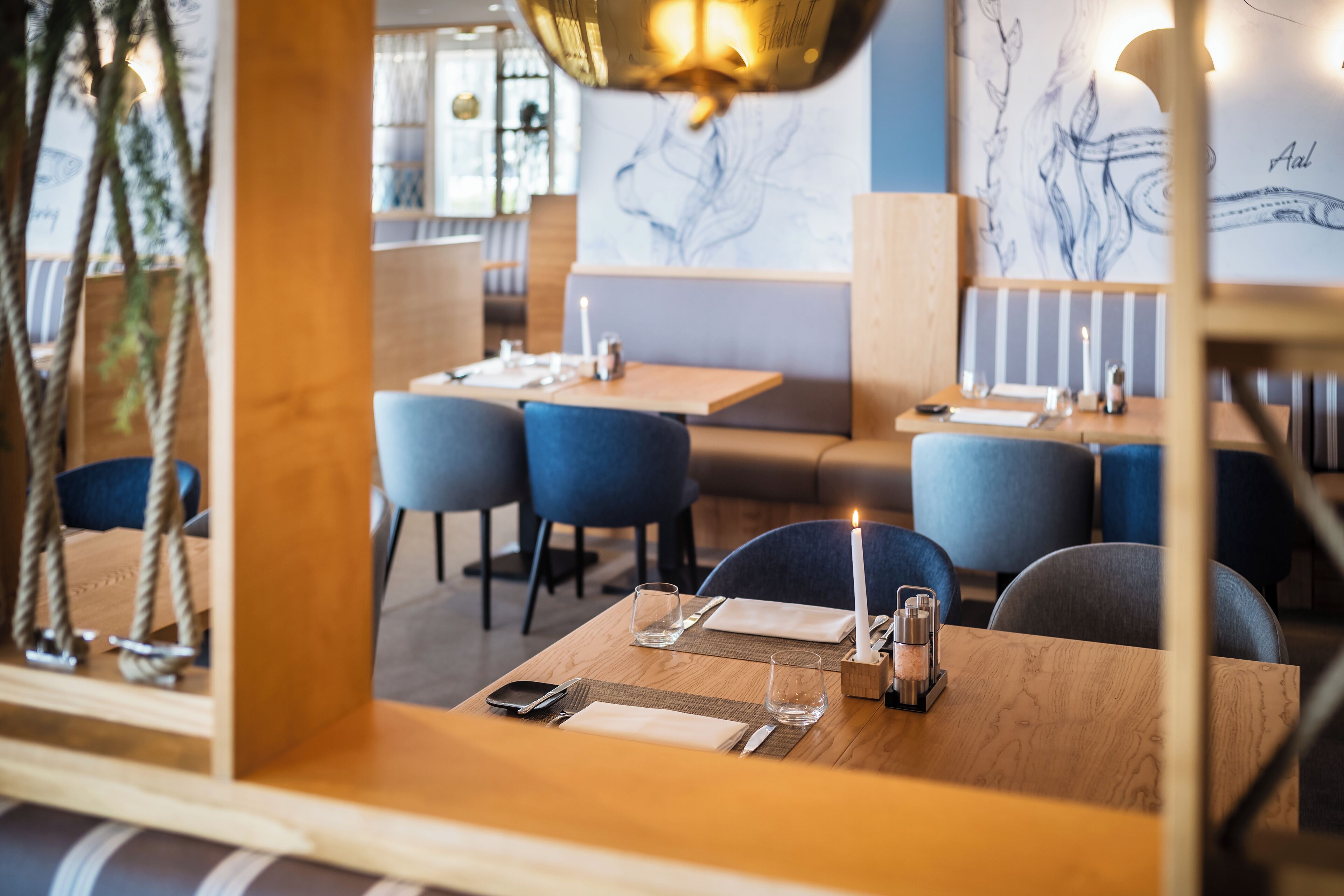 Ein Restaurantinneres mit Holztischen, blauen Stühlen und einer Kerze auf jedem Tisch.