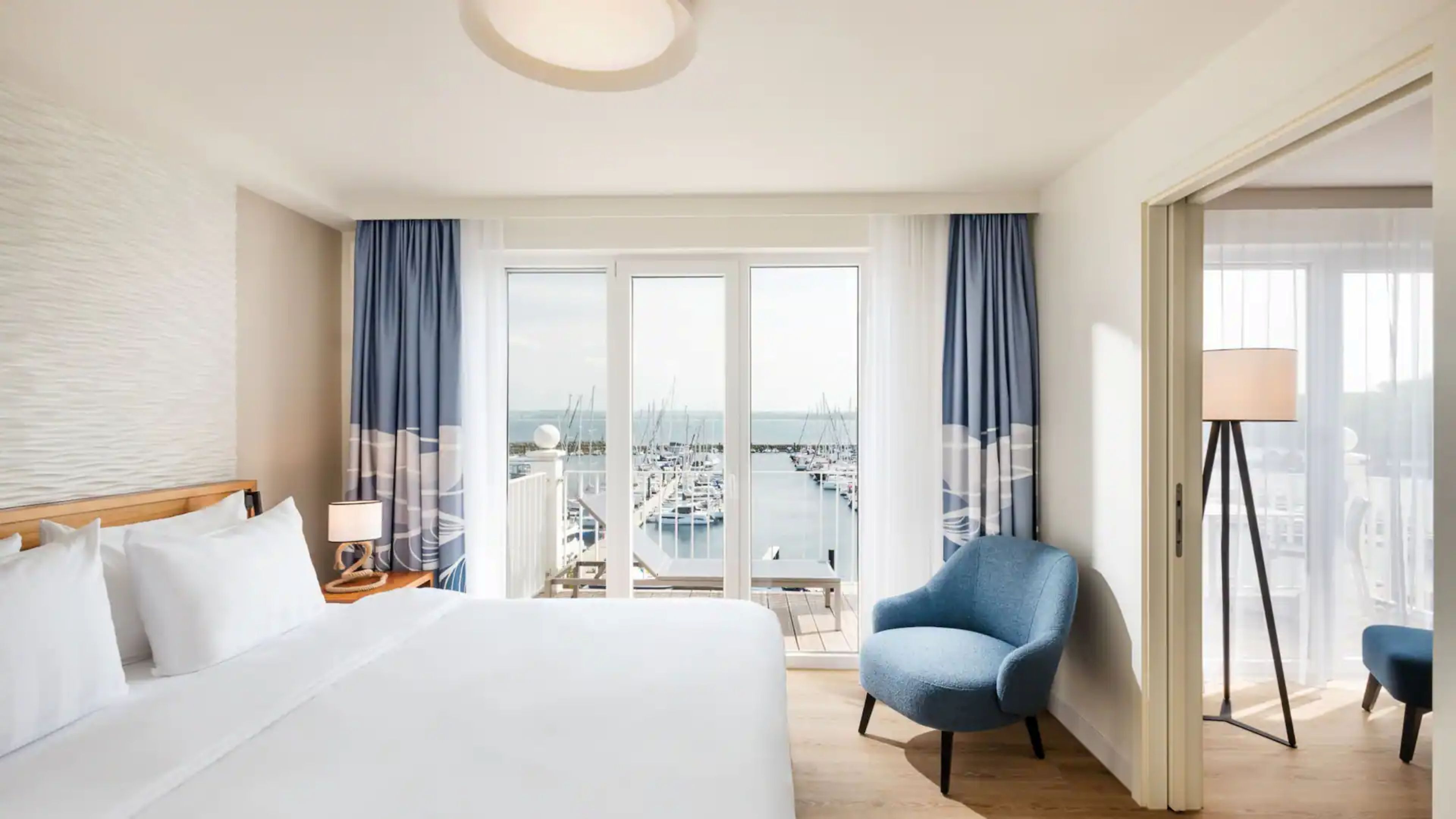A hotel room with a large bed, a chair, a lamp, and a view of a marina.
