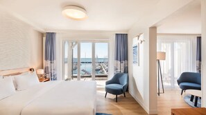 A hotel room with a bed, two armchairs, a desk, a lamp, and a view of the marina. - MAREBALTIC (Boltenhagen)