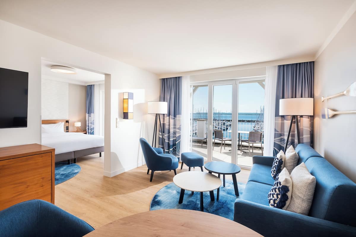 A modern hotel room with a bed, a desk, a sofa, and a balcony with a view of the city.