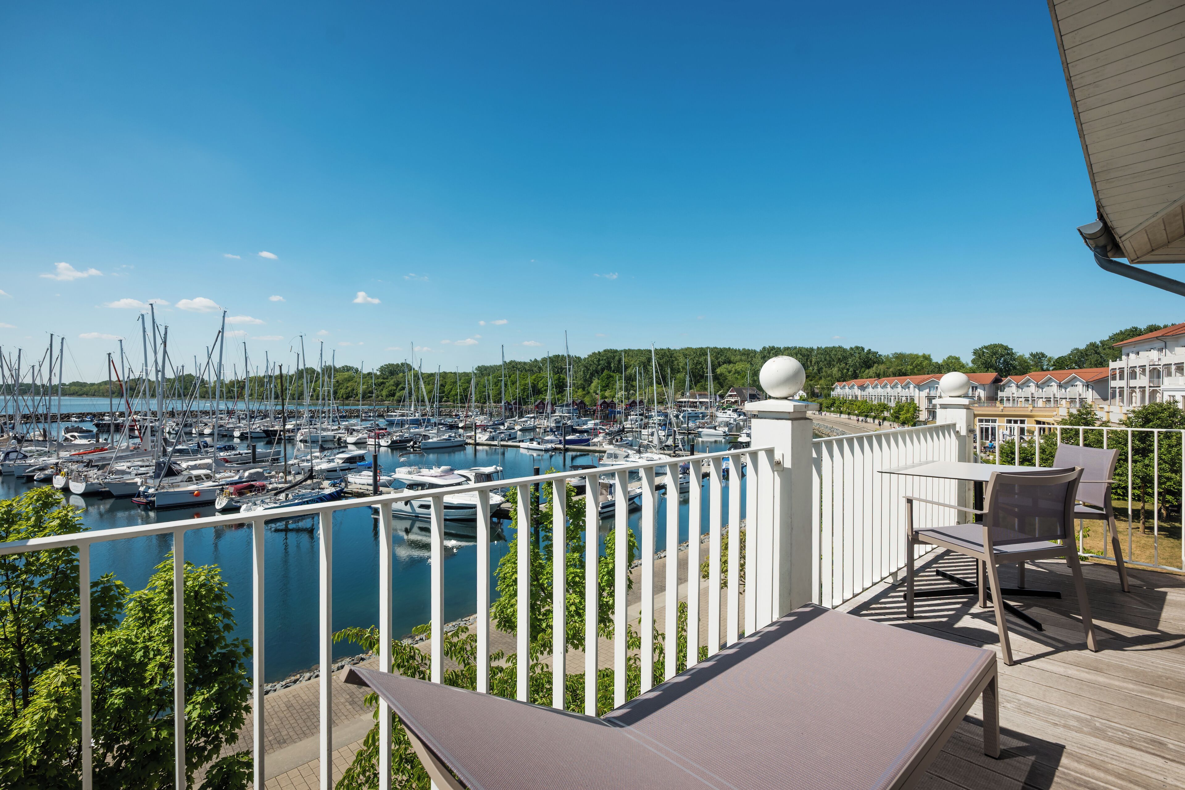 Ein Balkon mit Blick auf einen Hafen, Gartenmöbel und einem weißen Geländer.