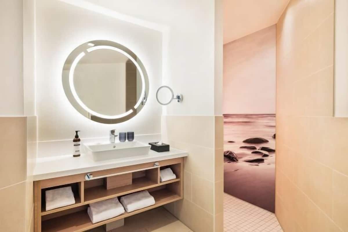 A modern bathroom with a round mirror, white sink, and wooden vanity.