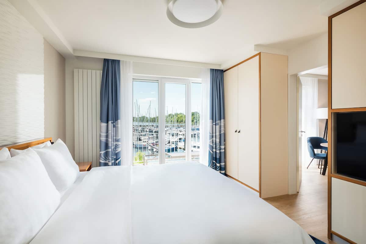A hotel room with a large bed, a view of a marina, and a TV.