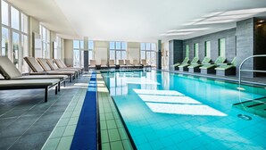 A large indoor swimming pool with lounge chairs and a view of the outside.