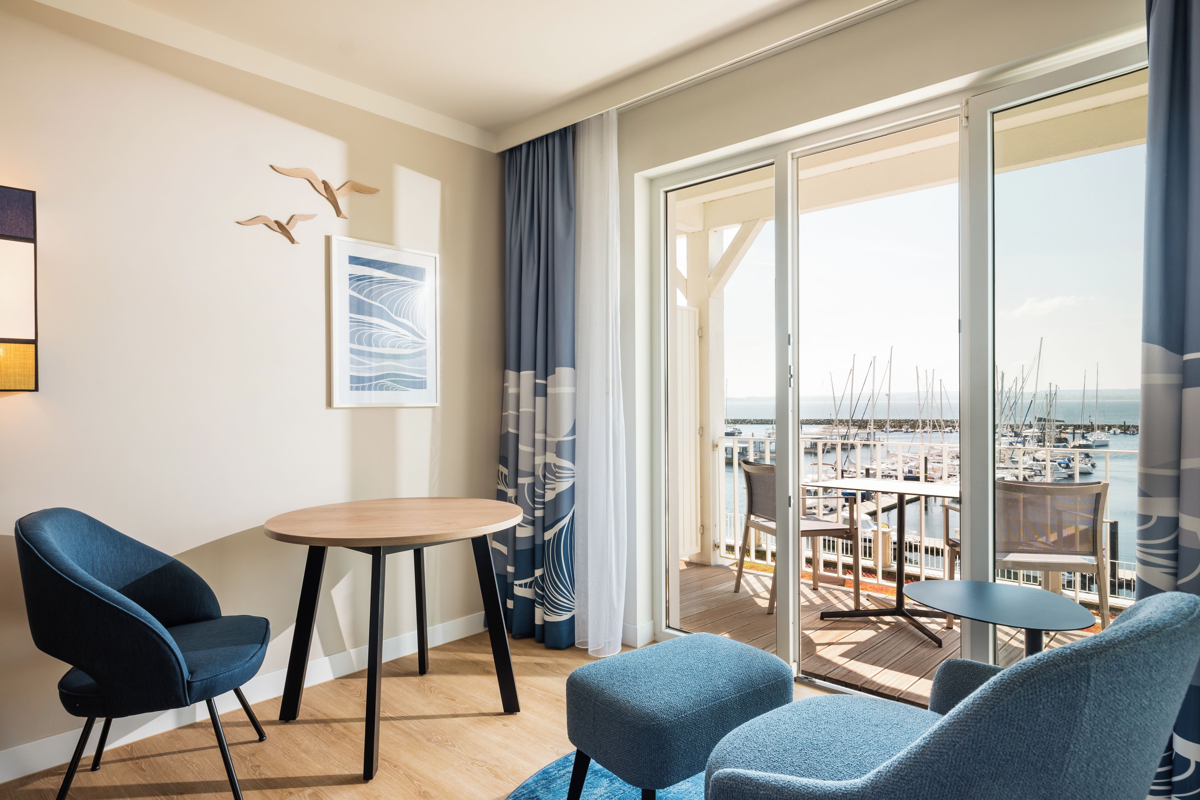 Una habitación moderna con balcón, una mesa redonda, dos sillas y vista a un puerto deportivo.