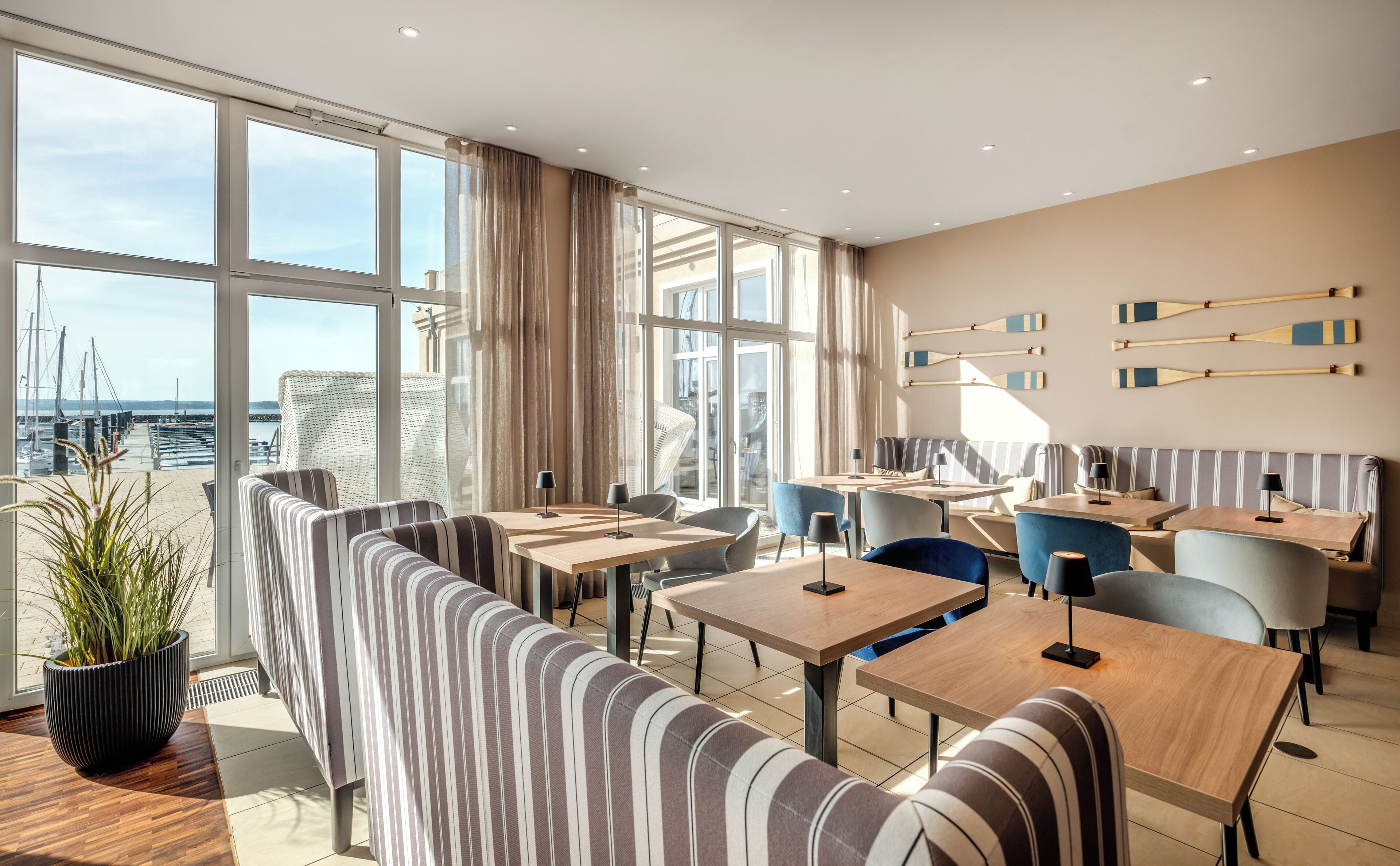 Ein modernes Hotelzimmer mit großen Fenstern, gestreifter Sitzgelegenheit und Blick auf den Yachthafen.