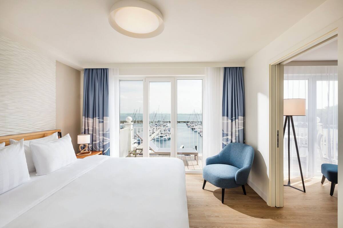A hotel room with a large bed, a chair, a lamp, and a view of a marina.
