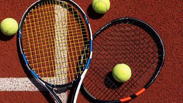 Two tennis rackets and three tennis balls on a red clay court.