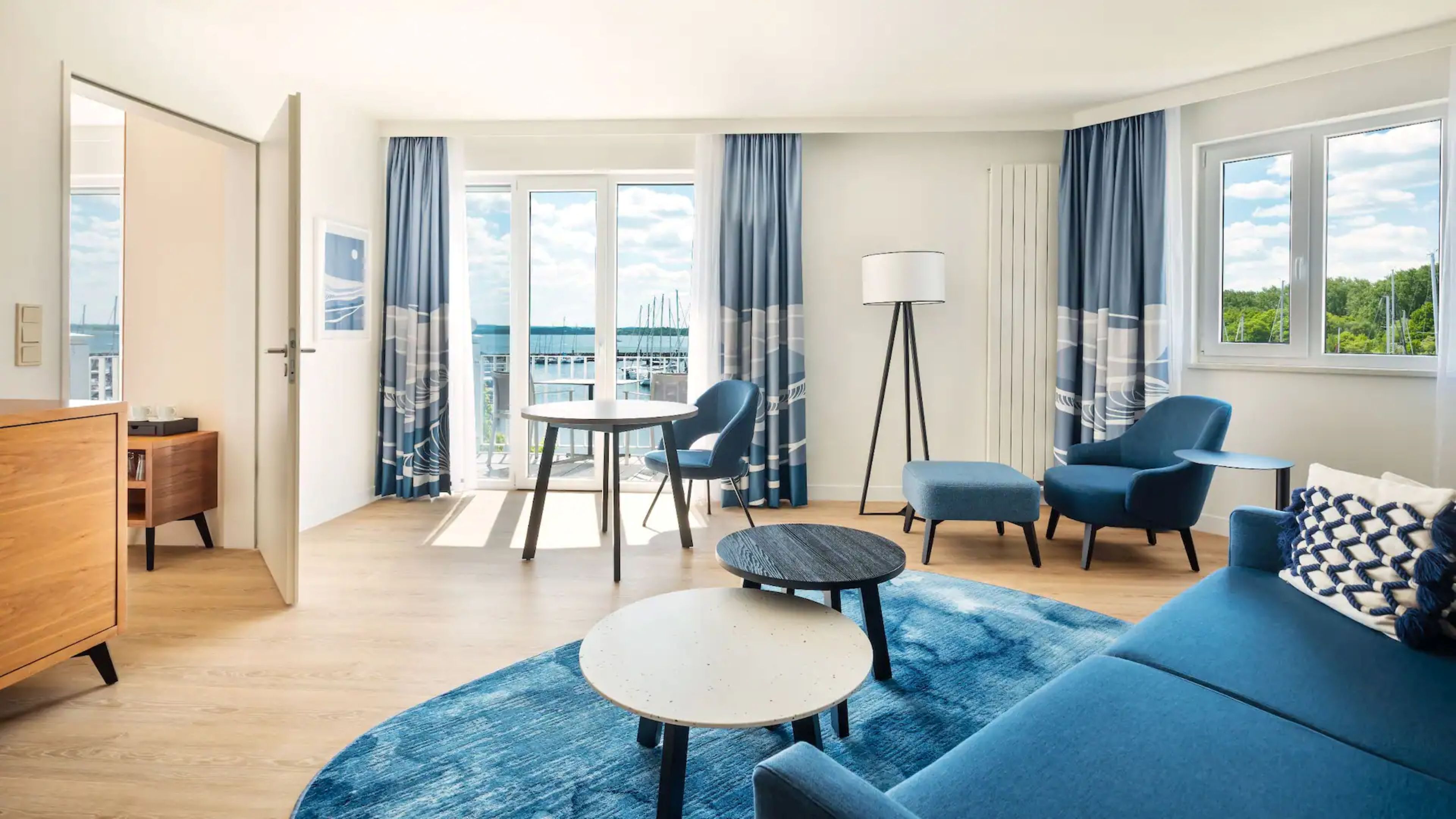 A modern living room with a sofa, chairs, a coffee table, and a view of the sea.