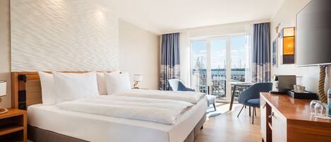 A hotel room with a large bed, a desk, a chair, and a view of the marina.