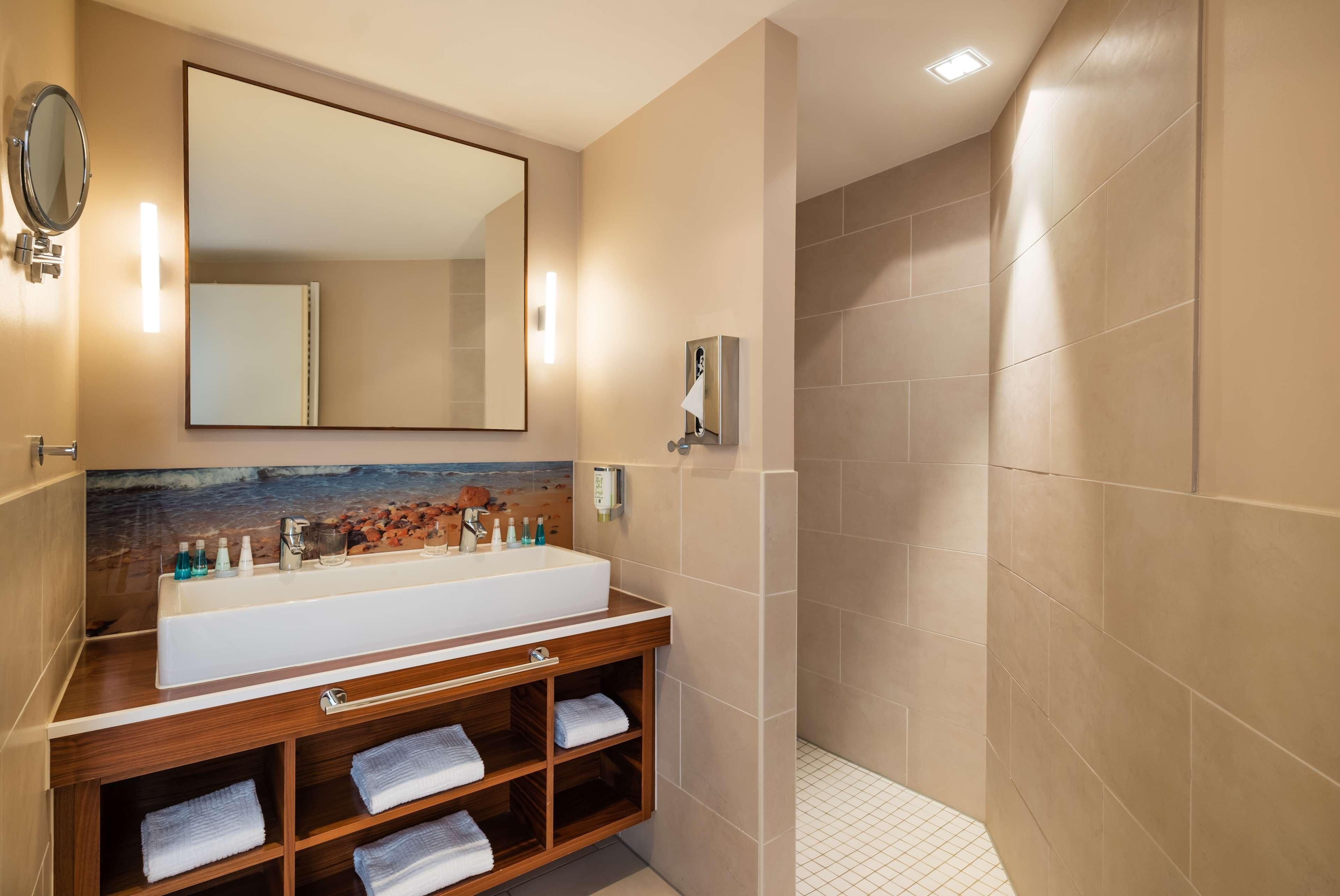 Un baño con un espejo grande, un lavamanos y una zona de ducha.
