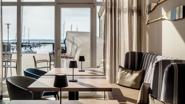 A modern interior with a view of the marina, featuring a sofa, chairs, a table, and lamps.