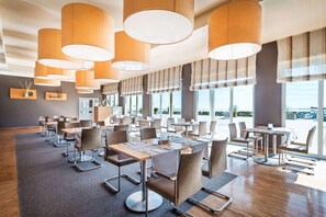 A modern dining area with multiple tables and chairs, large windows, and hanging pendant lights. - MAREBALTIC (Boltenhagen)
