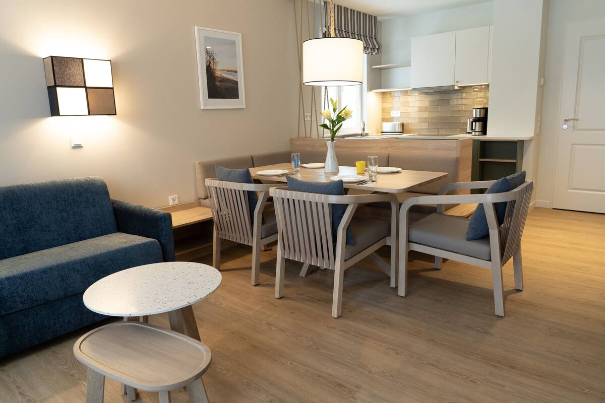 Uma sala de estar moderna com um sofá azul, uma mesa de centro redonda e uma área de jantar com mesa e cadeiras.