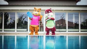 Dos mascotas posando junto a una piscina con un edificio moderno al fondo.