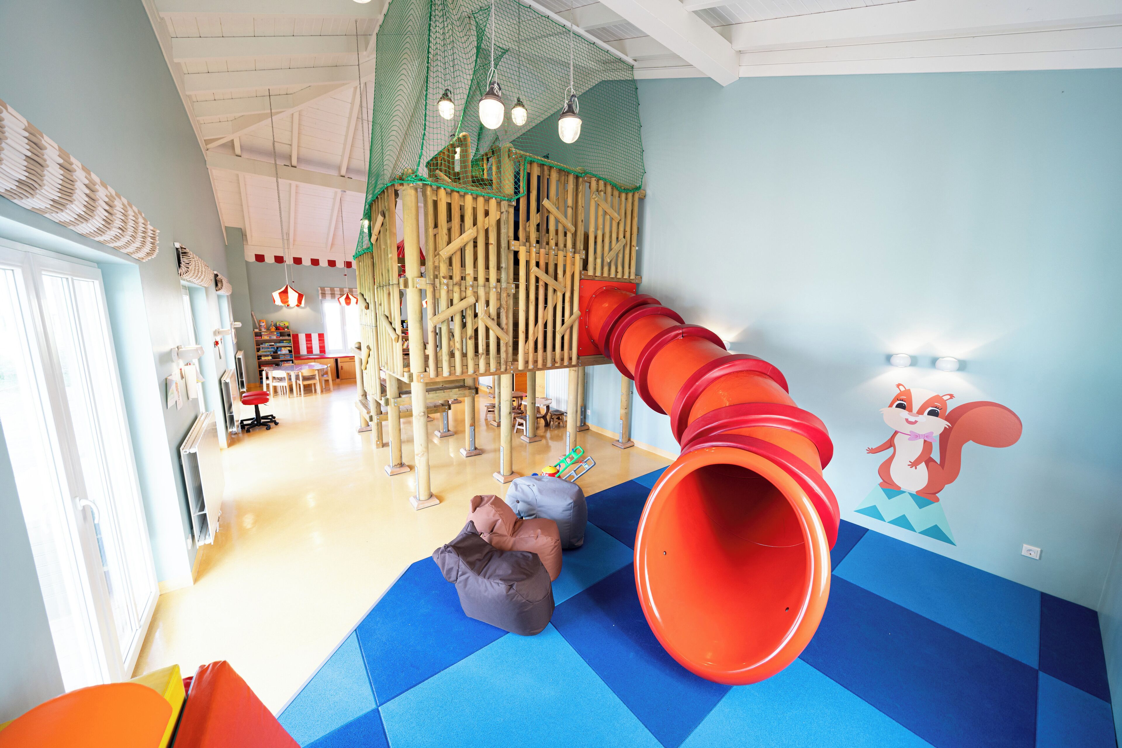 A children's play area with a slide, climbing structures, and soft play mats.
