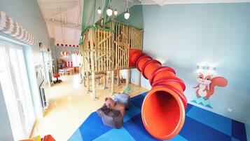 A children's play area with a slide, climbing structures, and soft play mats.