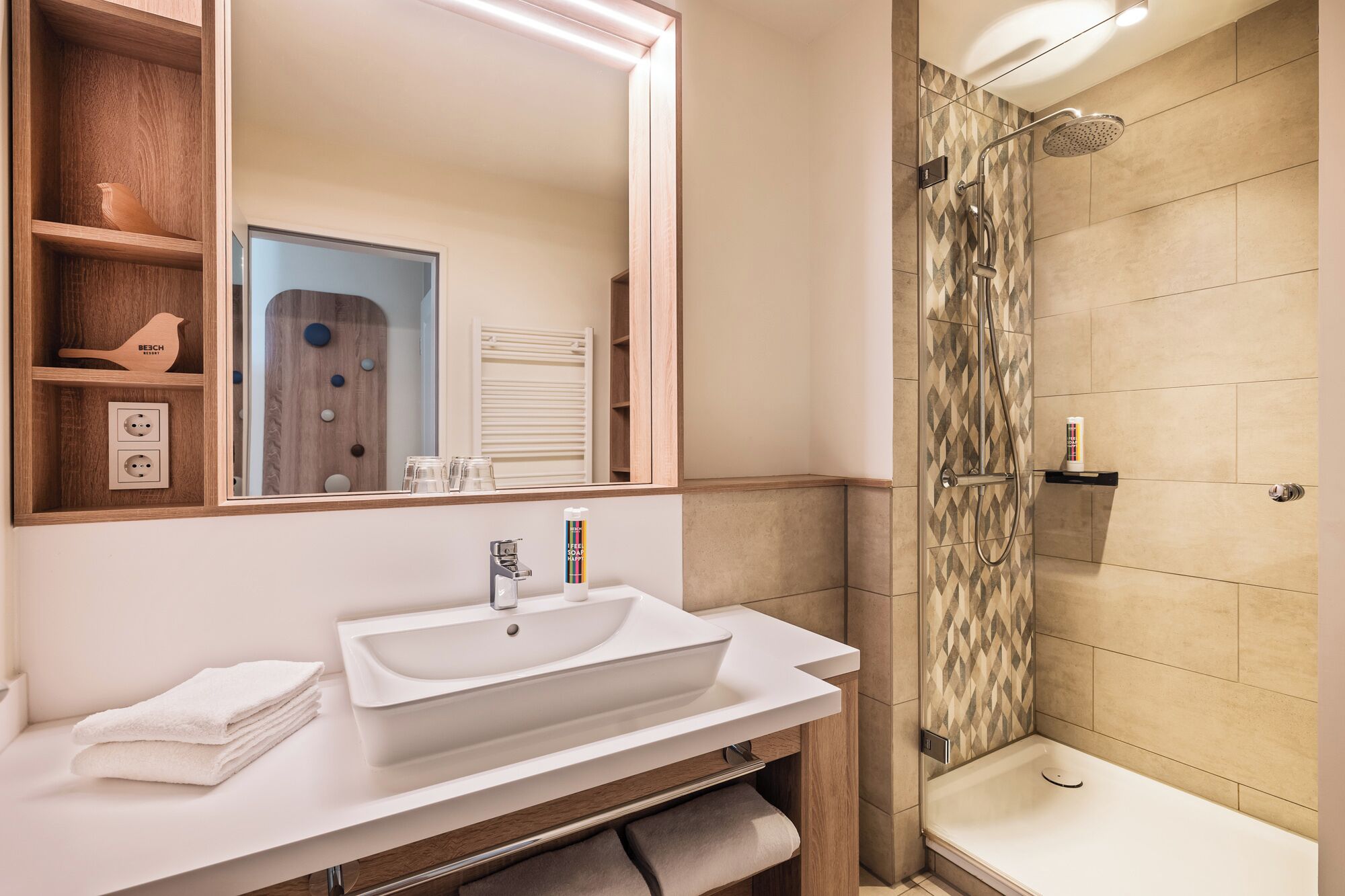 Un baño moderno con un espejo grande, lavamanos blanco y zona de ducha.