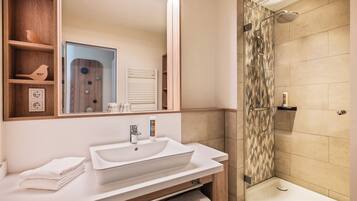 Un baño moderno con un espejo grande, lavamanos blanco y zona de ducha.
