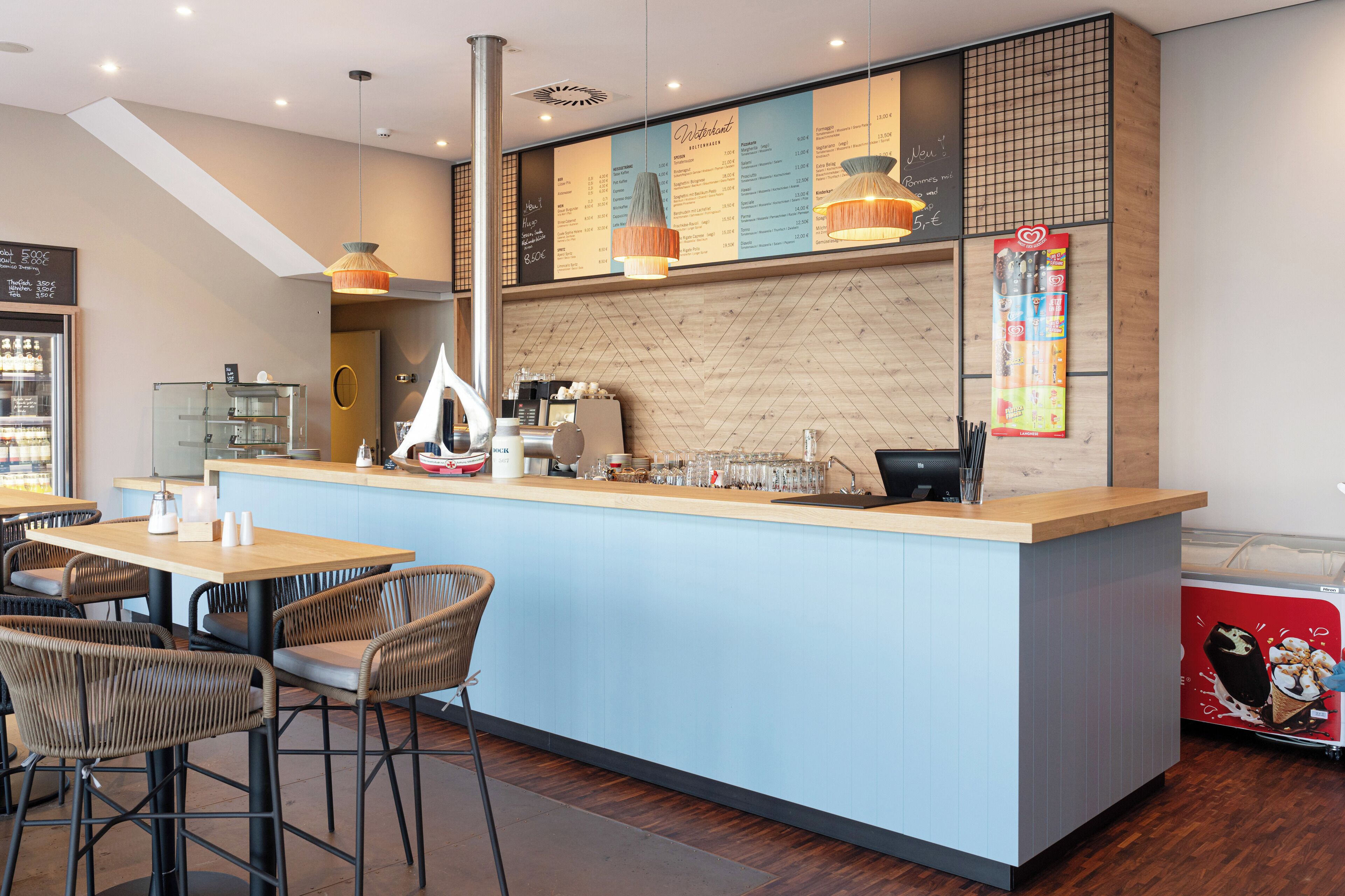 A modern cafe with a central counter, seating area, menu board, and a coffee machine.