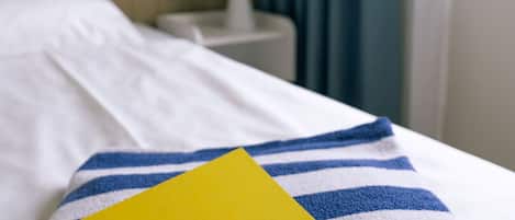 Une chambre d’hôtel avec un lit parfaitement fait, une serviette à rayures et un petit livret jaune intitulé « BEECH Resort » posé sur le lit.