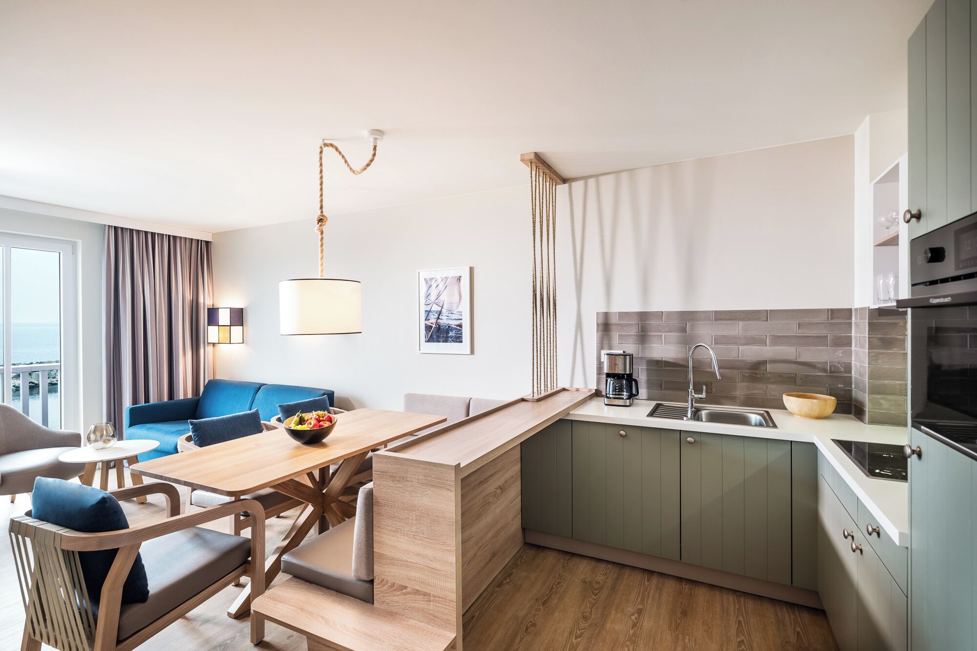 A compact kitchen with a dining area, a coffee machine, and a view of the sea through the window.