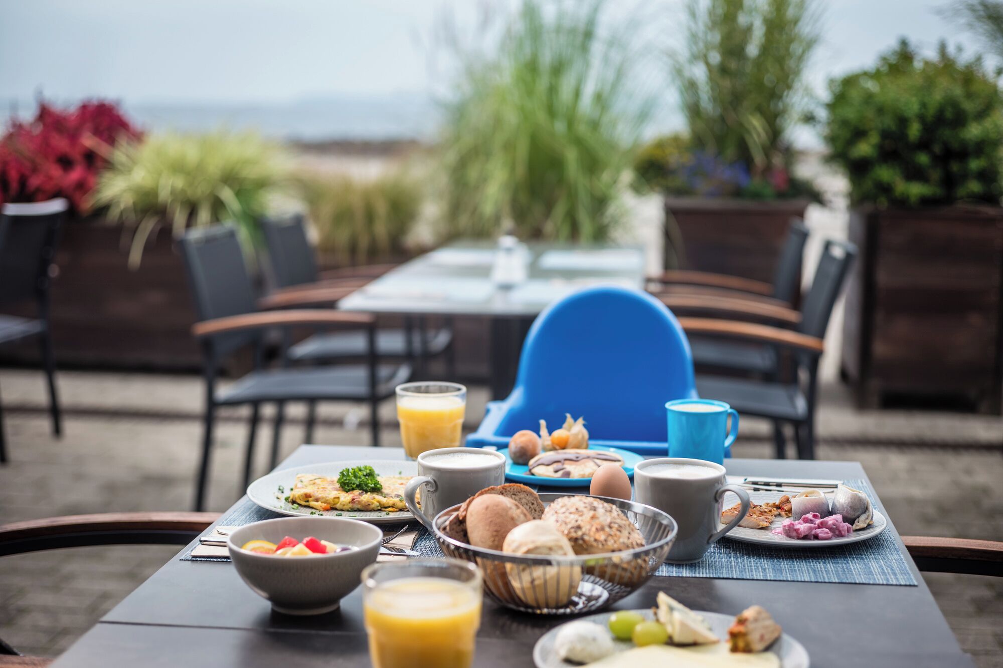 Un espace de restauration en plein air avec une table dressée pour le petit-déjeuner, comprenant des assiettes de nourriture, un saladier de fruits et une tasse de café.